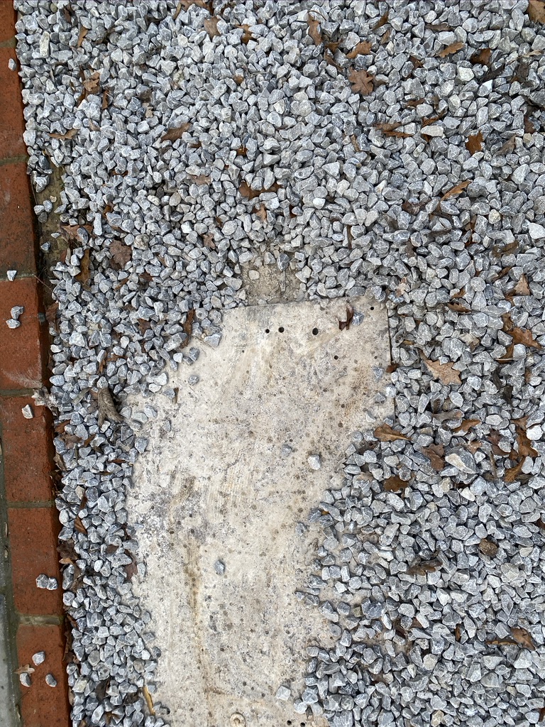 A leaking inspection chamber cover with holes in and poorly fitted and covered in gravel. 