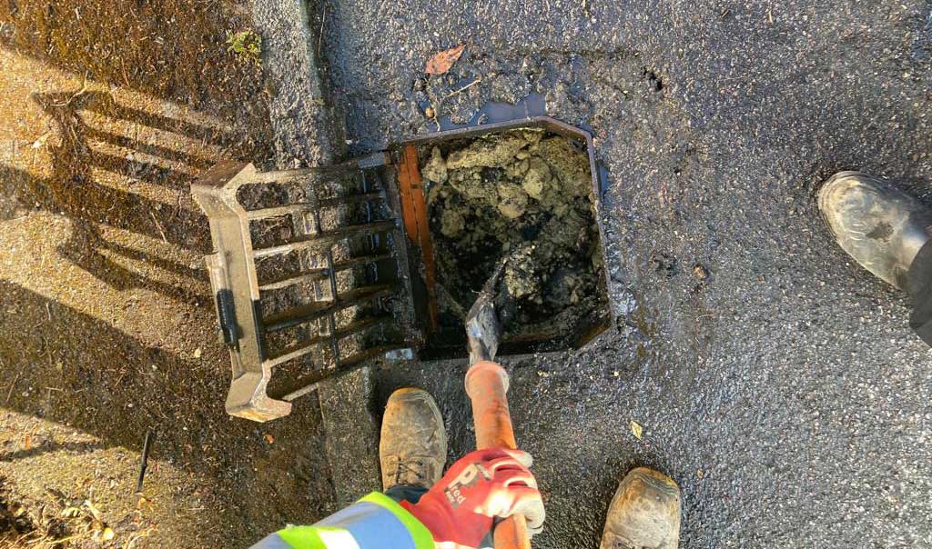 A picture of a blocked road gully that needs gully sucking to clear it.
